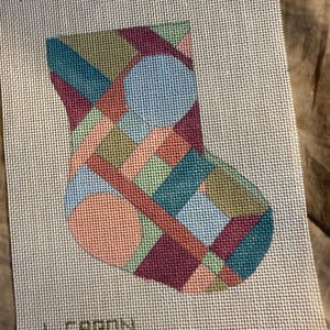 May include: A needlepoint canvas featuring a colorful patchwork design in the shape of a stocking. The design incorporates squares and circles in shades of teal, pink, blue, green, and burgundy. The text "PATCHWORK" and "L. CARON" are visible.