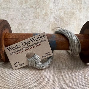 May include: A spool of gray cotton floss labeled "Weeks Dye Works" with the color number 1174 and the name "Tin Roof". The label also states "Specializing in Hand Over Dyed Fibers" and "Floss Collection".