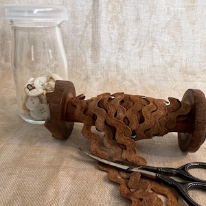 May include: A spool of brown wavy trim with a wooden base and a pair of scissors. The trim is wound around the spool and is ready to be cut.