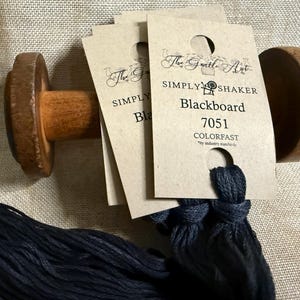 May include: Wooden thread holder with several cards of black thread labeled "Blackboard 7051 COLORFAST" by The Gentle Art. The thread is a dark navy blue color. The holder is made of light brown wood.