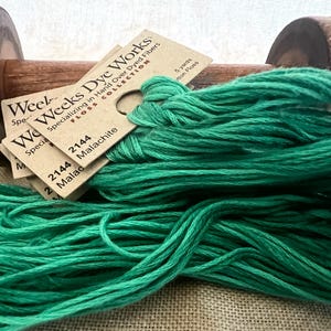 May include: A spool of Weeks Dye Works floss in the color Malachite, a vibrant green. The spool is labeled with the color number 2144 and the name Malachite. The floss is 5 yards long.