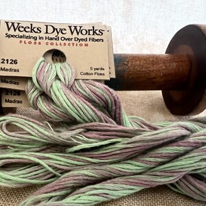 May include: A skein of green and pink hand-dyed cotton floss, labeled "Weeks Dye Works" and "2126 Madras". The floss is wound around a wooden spool.