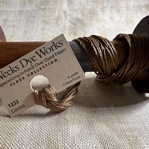 May include: A spool of brown cotton floss with a label that reads "Weeks Dye Works" and "Specializing in Hand Over Dyed Fibers" with the number "1233" and the word "Cocoa" printed on it.