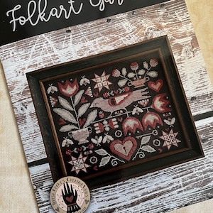 May include: Folkart Garden cross stitch pattern featuring a framed design with a red heart, birds, flowers, and stars. The pattern is by Teresa Kogut's Creative Stitches.