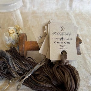 May include: A skein of brown embroidery floss with a tag that reads "The Gentle Art Simply Shaker Garden Gate 7067 Colorfast".