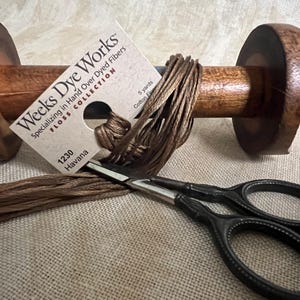 May include: A spool of brown embroidery floss wound around a wooden bobbin with a label that reads "Weeks Dye Works FLOSS COLLECTION Specializing in Hand Over Dyed Fibers 1230 Havana 5 yards Cotton Floss".