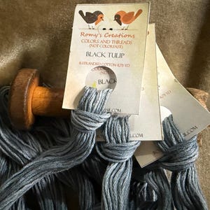 May include: Close-up of black cotton thread spools with tags. The tags read "Romy's Creations COLORS AND THREADS" and "BLACK TULIP". The thread is 6-stranded cotton, 8.75 yards. A wooden spool is visible.