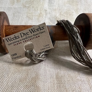 May include: A spool of Weeks Dye Works hand-dyed cotton floss in the color Pamlico, number 1259. The floss is a light brown color and is wound around a wooden spool. The spool is labeled with the Weeks Dye Works logo and the color name and number.