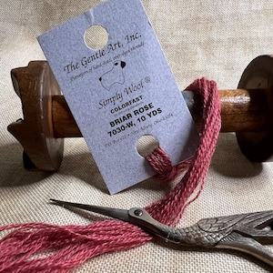 May include: A spool of red wool yarn with a label that reads "The Gentle Art, Inc. Simply Wool Colorfast by industry standards Briar Rose 7030-W, 10 YDS P.O. Box 670 New Albany, Ohio 43054"
