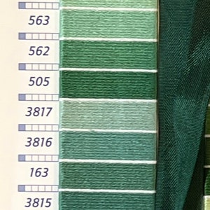 May include: A color chart of green embroidery floss threads, with various shades from light to dark. Each color is labeled with a number. A dark green ribbon is on the right side.