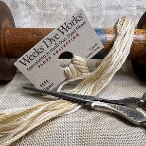 May include: A spool of beige cotton floss with a label that reads "Weeks Dye Works Floss Collection Specializing in Hand Over Dyed Fibers 1111 Fawn 5 yards Cotton Floss".