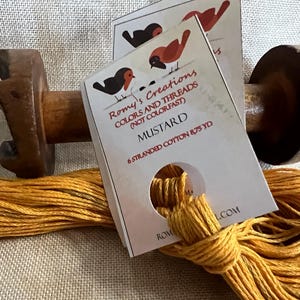 May include: A spool of mustard yellow embroidery floss with a label that reads "Romy's Creations Colors and Threads (Not Colorfast) Mustard 6 Stranded Cotton 875 yd"