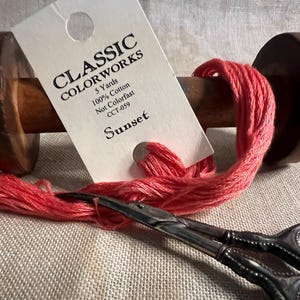 May include: A spool of red embroidery floss labeled "Classic Colorworks Sunset CCT-059 5 Yards 100% Cotton Not Colorfast" with a pair of embroidery scissors.