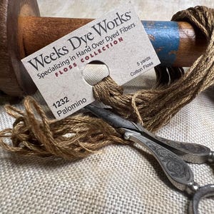 May include: A spool of brown cotton floss labeled "Weeks Dye Works Floss Collection 1232 Palomino 5 yards Cotton Floss".