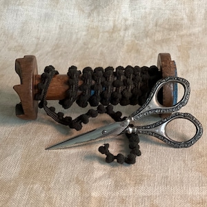 May include: A spool of black pom-pom trim with a wooden spindle and a pair of ornate silver scissors.