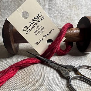 May include: A spool of red embroidery floss with a label that reads "CLASSIC COLORWORKS 5 Yards 100% Cotton Not Colorfast CCT-136 Ruby Slippers".