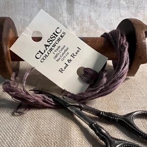 May include: A wooden spool of purple thread with a label that reads "CLASSIC COLORWORKS 5 Yards 100% Cotton Not Colorfast CCT-116 Rod & Reel".
