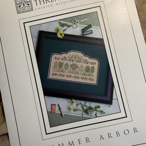 May include: A pattern booklet titled The Drawn Thread Charted Needlework Designs Summer Arbor. The cover features a framed cross-stitch sampler with green trees and floral motifs, accompanied by small scissors, thread spools, and a needle case.