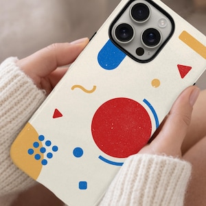 May include: A phone case with a cream background and a colorful geometric design. The design includes a large red circle, blue and yellow shapes, and small red triangles. The case is held in a person's hands.