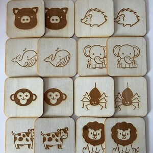 Peut inclure: Ensemble de carreaux carrés en bois avec des illustrations d'animaux gravées. L'ensemble comprend des images de cochon, hérisson, baleine, éléphant, singe, araignée, vache et lion. Les carreaux sont brun clair avec des détails gravés brun foncé.