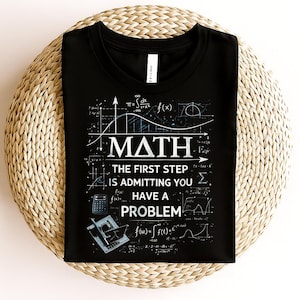 May include: Black t-shirt with a white graphic design featuring mathematical equations and the word "MATH". The text "THE FIRST STEP IS ADMITTING YOU HAVE A PROBLEM" is also included in the design. The shirt is displayed on a woven surface.