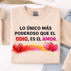 May include: Beige sweatshirt with the text "LO ÚNICO MÁS PODEROSO QUE EL ODIO, ES EL AMOR." in black and red. The design includes a broken heart and two pink hearts with a rainbow-colored streak.