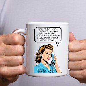 May include: White ceramic mug with a retro comic book style illustration of a woman on the phone. The speech bubble says, "HELLO POLICE... THERE'S A MAN OUTSIDE IN A LONG COAT, GREY HAT, SMOKING A CIGARETTE.."