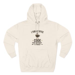 May include: Cream-coloured hoodie with a front pocket and drawstring hood. The graphic on the front reads "I Turn Coffee Into Code Food Without A Trace" with a coffee cup illustration. A casual, comfortable garment.