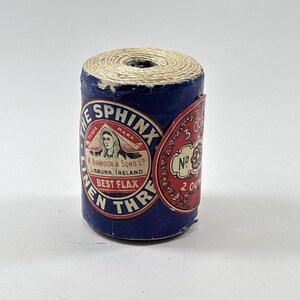 May include: A spool of The Sphinx brand linen thread with a blue paper label featuring a red circular emblem, a sphinx illustration, and the text W. Barbour & Sons Ltd, Lisburn, Ireland, Best Flax, No 3 Cord, and 2 Ounces.