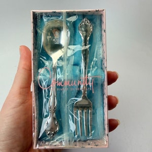 May include: A boxed set of Community silverware, including a spoon and fork. The silver-colored utensils are in a pink and blue box with the words "Community Fine Silverplate" printed on the front. The spoon and fork have ornate handles.