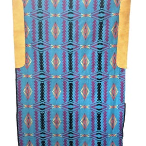 May include: A turquoise blanket with a geometric pattern in black, purple, orange, and yellow. The blanket has two tan leather pockets on either side. The blanket is held up by two hands.