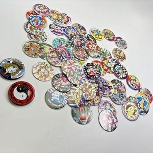 May include: A collection of numerous circular cardboard game discs, commonly known as pogs, featuring various colorful graphic illustrations, holographic finishes, and cartoon characters, including one distinct red disc with a black and white yin-yang symbol.