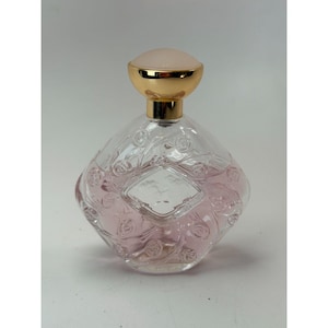 May include: A clear, diamond-shaped perfume bottle with a gold-colored cap and a light pink liquid inside. The bottle has a decorative floral pattern and a blank, diamond-shaped label on the front. The cap is a light pink color.