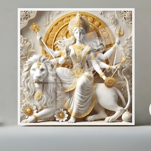 Puede incluir: Una obra de arte enmarcada representa una escultura blanca y dorada de una deidad montada en un león. La deidad tiene múltiples brazos y lleva una corona. El fondo presenta patrones ornamentados y texturizados. La obra se exhibe sobre una superficie gris.