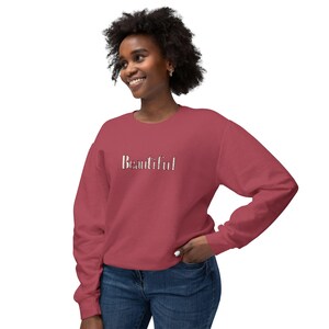 Puede incluir: Una sudadera granate con la palabra "Beautiful" en blanco, con una fuente estilizada en el pecho. La parte superior de manga larga está hecha de un material suave y la lleva una persona.