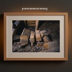 May include: Framed print featuring a dimly lit interior with stacked wooden blocks, possibly in a mine or storage area. The blocks have text on them. The frame is light wood, and the text "KENNERUNDERGROUND" is at the top.
