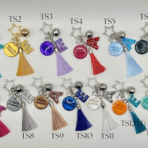 May include: A collection of keychains with star-shaped charms, letter accents, and colorful tassels. Each keychain features a different color scheme, including teal, gold, purple, red, blue, black, pink, silver, brown, and orange. Some keychains have text that reads "Taylor's Version".