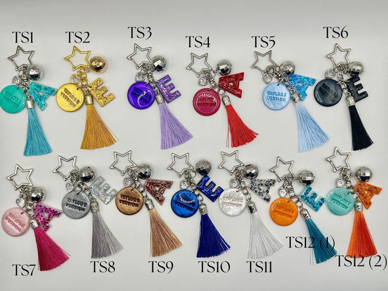 May include: A collection of keychains with star-shaped charms, letter accents, and colorful tassels. Each keychain features a different color scheme, including teal, gold, purple, red, blue, black, pink, silver, brown, and orange. Some keychains have text that reads "Taylor's Version".