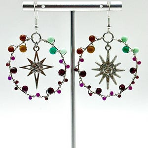 May include: A pair of silver-toned hoop earrings featuring a central eight-pointed star charm encrusted with clear rhinestones. The wire hoops are decorated with small, multi-colored beads in shades of purple, red, orange, yellow, and green.