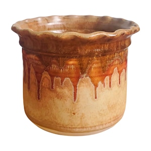 May include: A handcrafted ceramic pot with a ruffled rim. The pot features a warm color palette, with a light beige base and rich brown and orange dripping glaze. The design is reminiscent of rustic pottery.