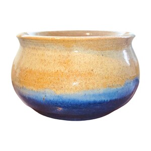 May include: A handmade ceramic bowl with a rounded shape. The bowl features a color gradient, transitioning from a light tan at the top, through a golden yellow middle, to a deep blue at the base. The rim is slightly flared.