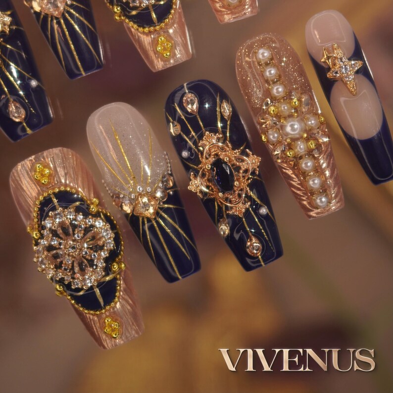 May include: A collection of long, decorated artificial nails. Designs feature navy blue, gold, and rose gold hues with intricate patterns, rhinestones, and pearls. The nails display various shapes and decorative elements, with the word "VIVENUS" at the bottom.