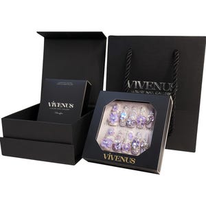 May include: Black gift set featuring artificial nails with purple flower and rhinestone embellishments. The set includes a box of nails, a small box, and a shopping bag. The text "VIVENUS Luxury Nail Gallery" is visible.