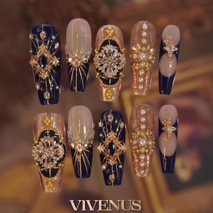 May include: A collection of ten long, coffin-shaped false nails. Designs include navy blue, gold, and pearl embellishments. Some nails have detailed gold filigree, others a gradient effect. The brand name "VIVENUS" is displayed at the bottom of the image.