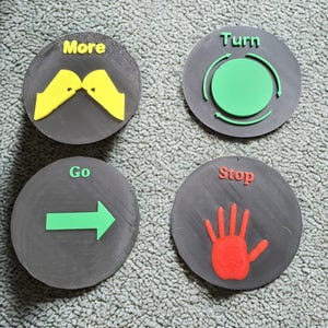 May include: Four gray circular buttons with raised text and graphics. The buttons say "More" with yellow shapes, "Turn" with a green circle and arrows, "Go" with a green arrow, and "Stop" with a red hand.