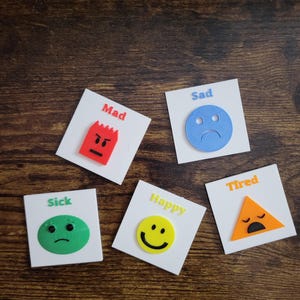 May include: Five square white tiles featuring colorful 3D shapes representing emotions. A red jagged shape labeled Mad, a blue circle labeled Sad, a green oval labeled Sick, a yellow circle labeled Happy, and an orange triangle labeled Tired.