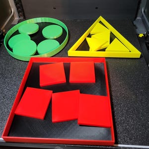 Może przedstawiać: Zbiór geometrycznych kształtów w jasnych kolorach. Zielona taca zawiera kilka zielonych kół. Żółty trójkąt zawiera żółte trójkąty. Czerwona taca zawiera czerwone kwadraty. Obiekty znajdują się na czarnej powierzchni.