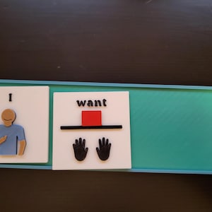 Puede incluir: Un tablero de comunicación con las palabras "Yo quiero" y los símbolos correspondientes. La sección "Yo" presenta una figura de persona, mientras que la sección "quiero" incluye un cuadrado rojo y dos símbolos de manos. El tablero es turquesa y está enmarcado en azul.