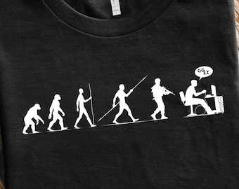May include: Black t-shirt featuring a white evolution graphic. The graphic depicts the evolution of man, ending with a person at a computer with the word "GGZ" in a speech bubble. The shirt is displayed on a woven surface.