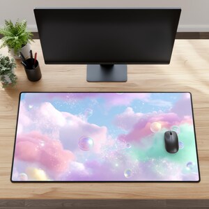 Op de afbeelding: Een rechthoekige bureaumuismat met een dromerig hemelontwerp met pastelroze, blauwe en groene wolken en iriserende bellen. Een zwarte computermuis ligt op de mat. De mat heeft een zwarte rand.